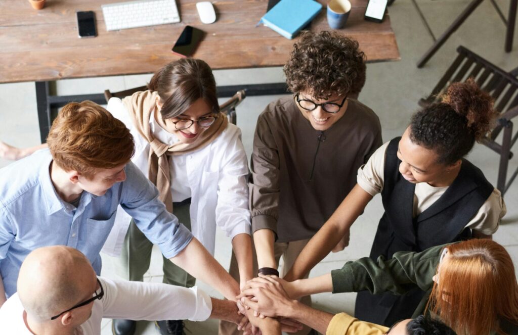 A diverse group of professionals joins hands in a team-building exercise indoors.